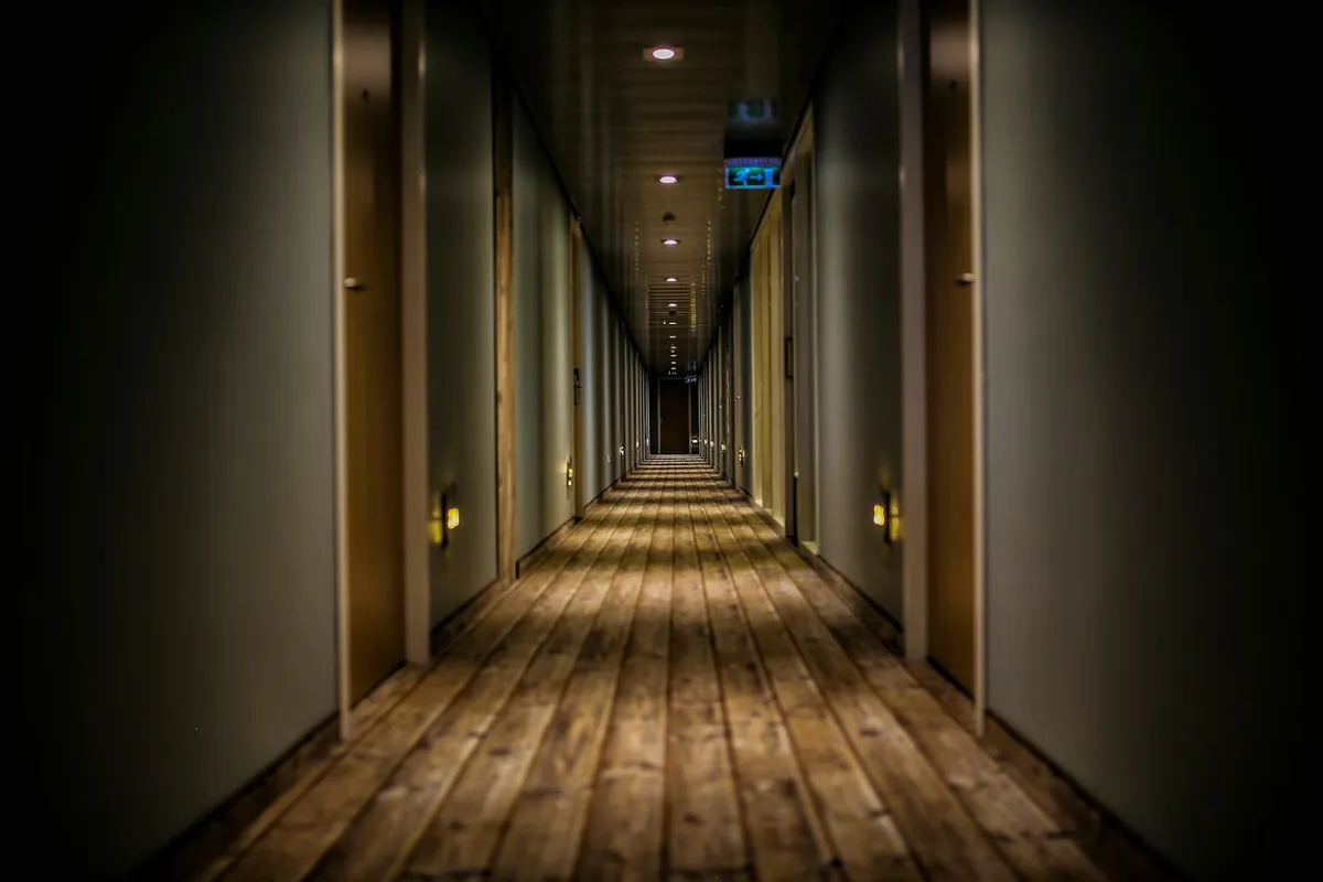 Long dark corridor with a lit ceiling and wooden floor