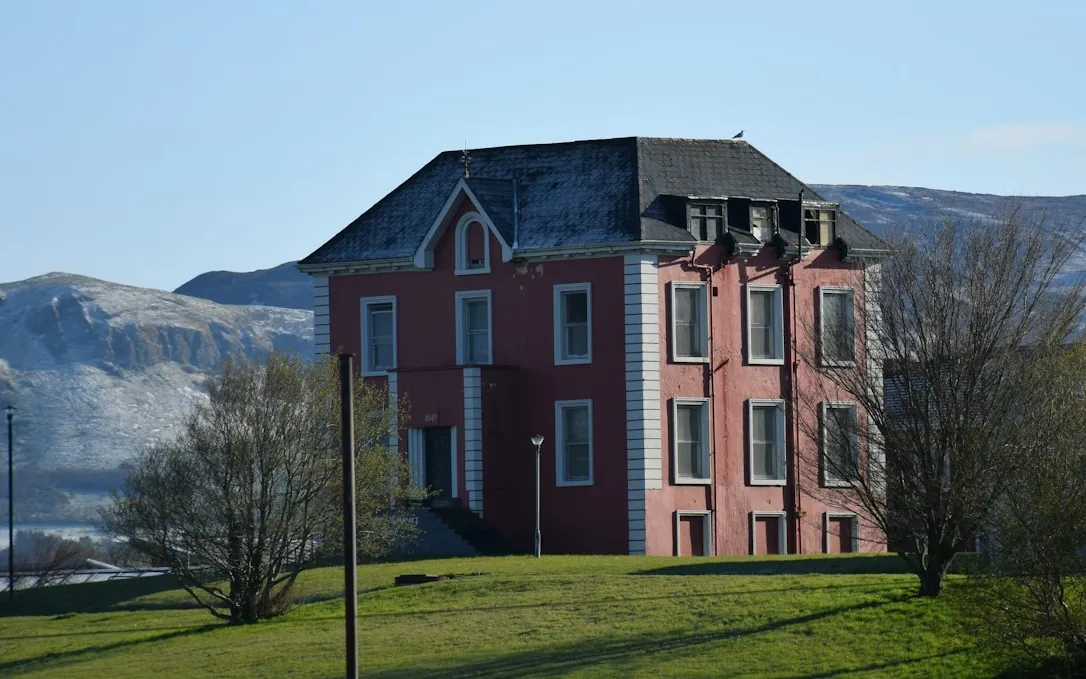 Red brick manor house with trees and mountains behind