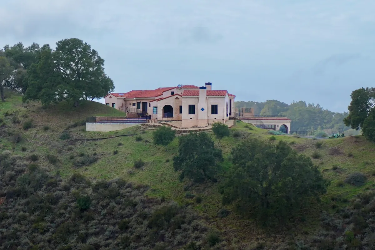 Large house on a green hillside with trees and a cloudy sky