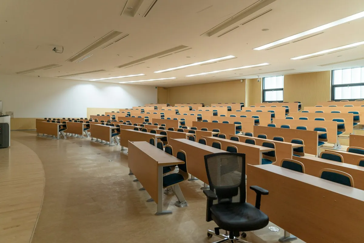 Large empty lecture hall with rows of wooden desks and black chairs