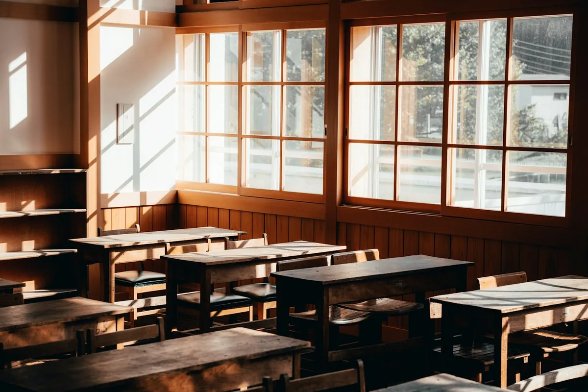 Sunlit classroom with large wooden-framed windows and dark wooden desks