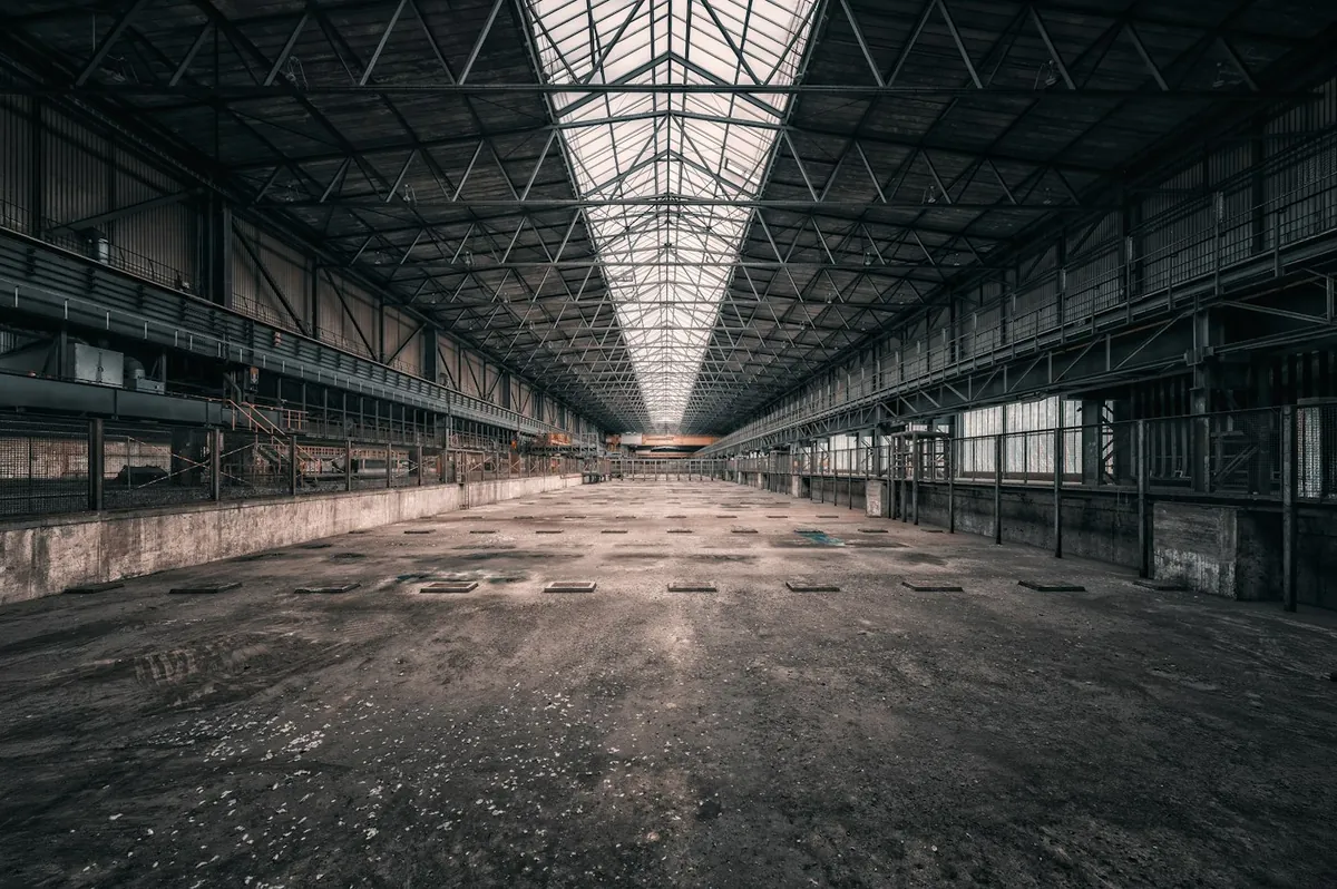 Vast empty industrial hall with a glass ridge roof and concrete floor