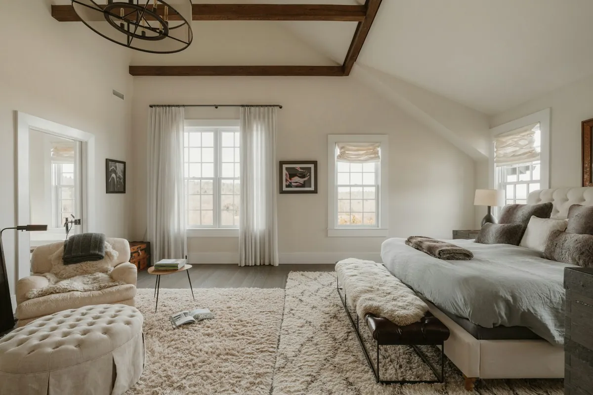 Bright bedroom with a white bed, rug and sitting area under exposed beams