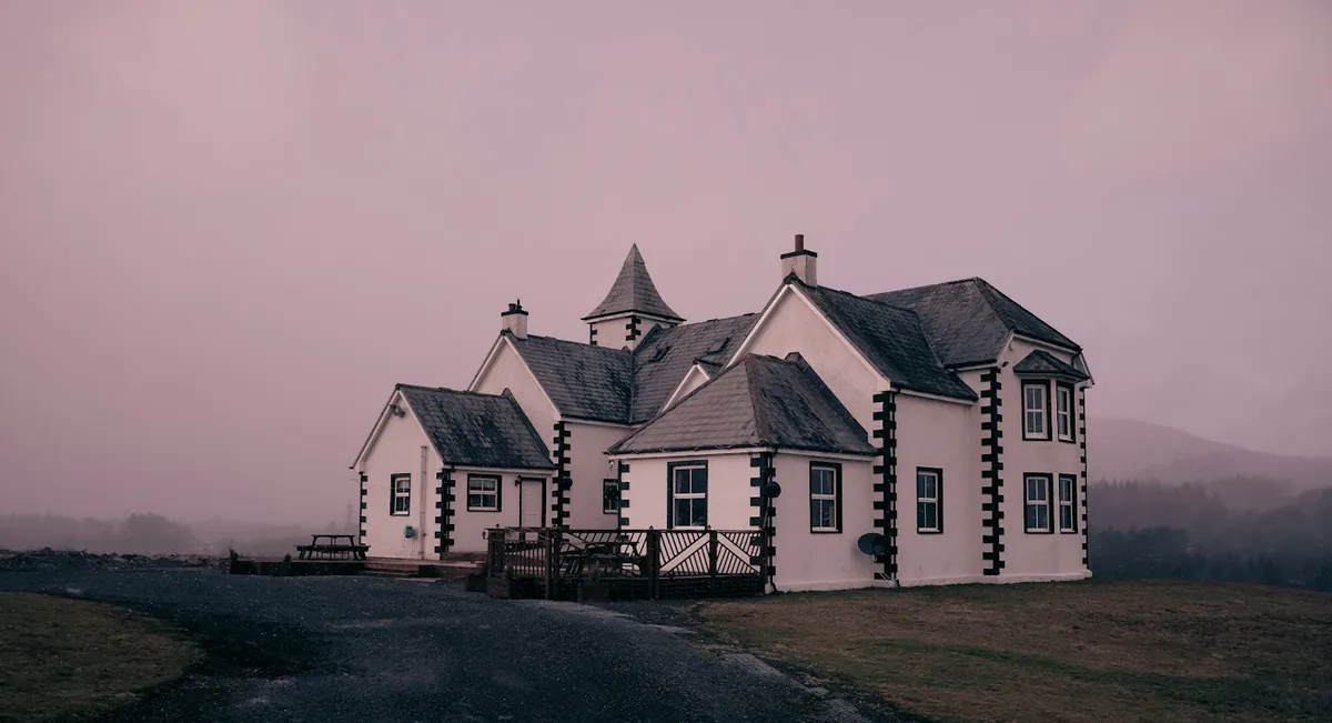 White gabled house on open land under a soft purple sky