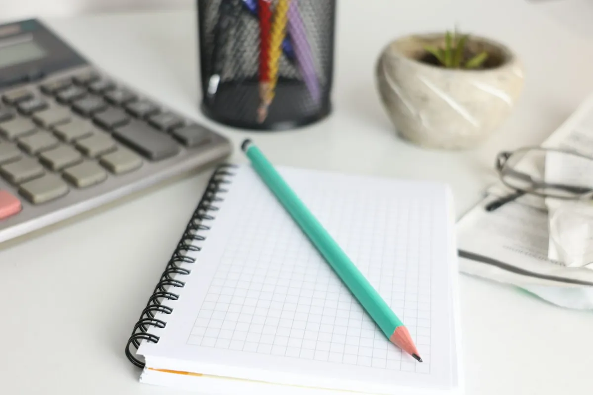 Desk with a calculator, notebook, pencil and a small plant