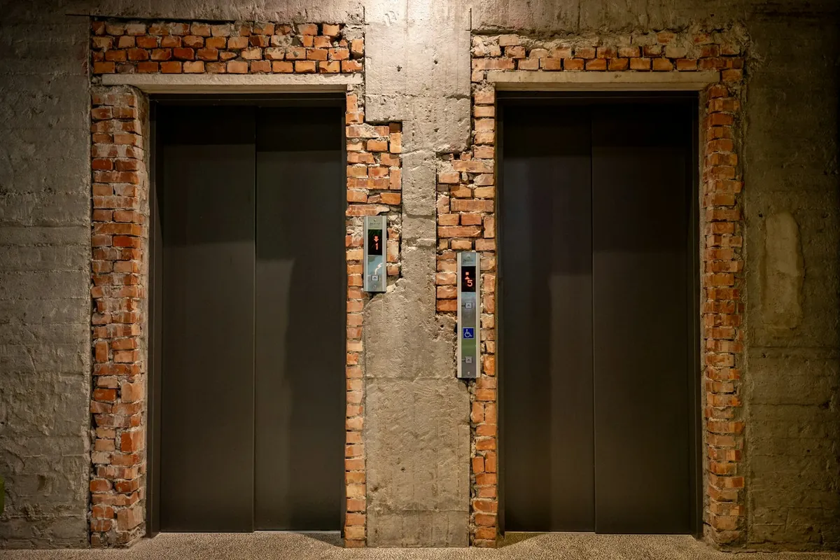 Two dark lift doors set in an exposed brick frame