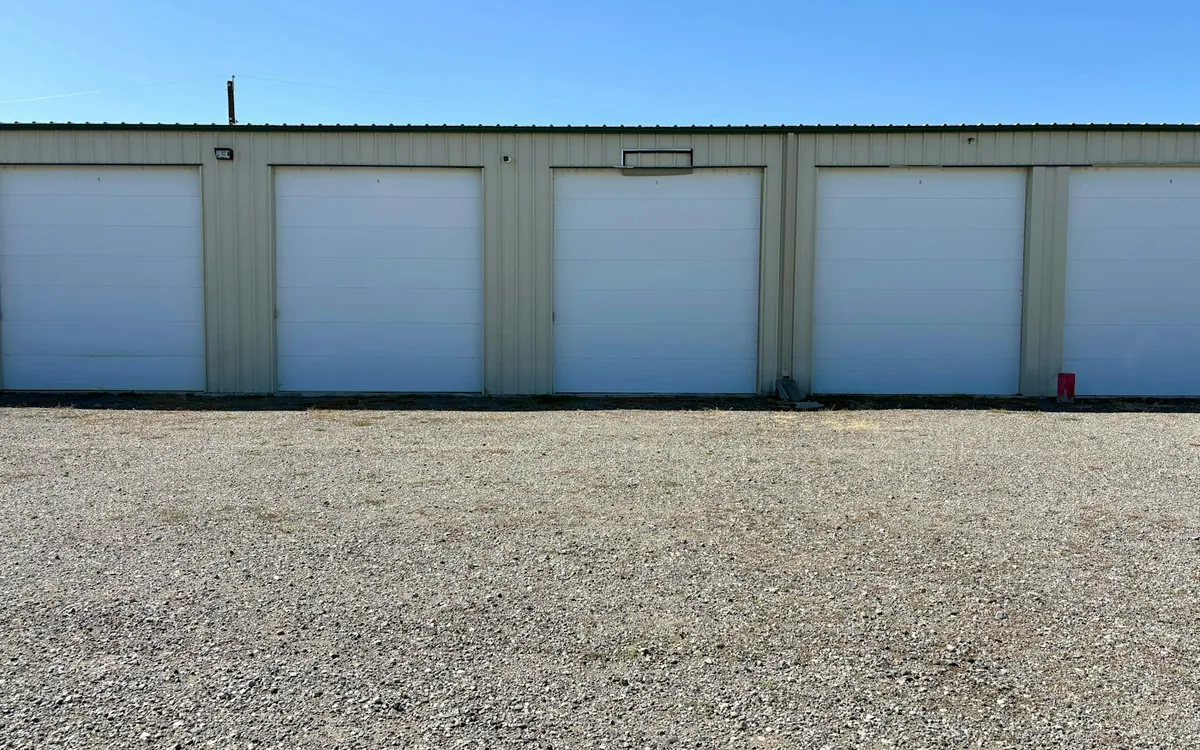 White roll-up doors on a long metal warehouse building above a gravel yard