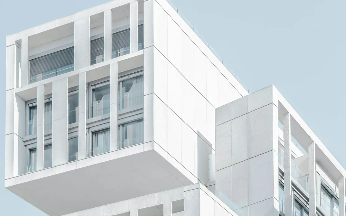 White modern building with stacked balconies against a pale blue sky