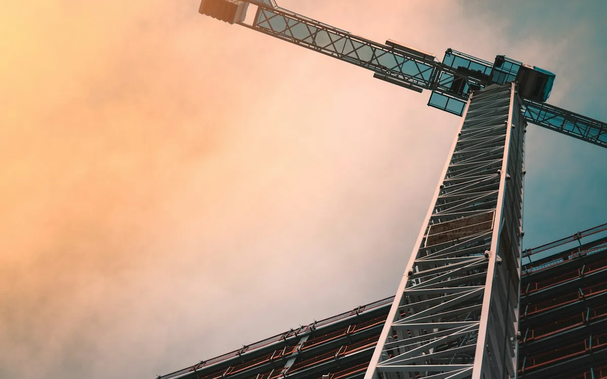 Tower crane silhouetted against a pink and orange sky above a building