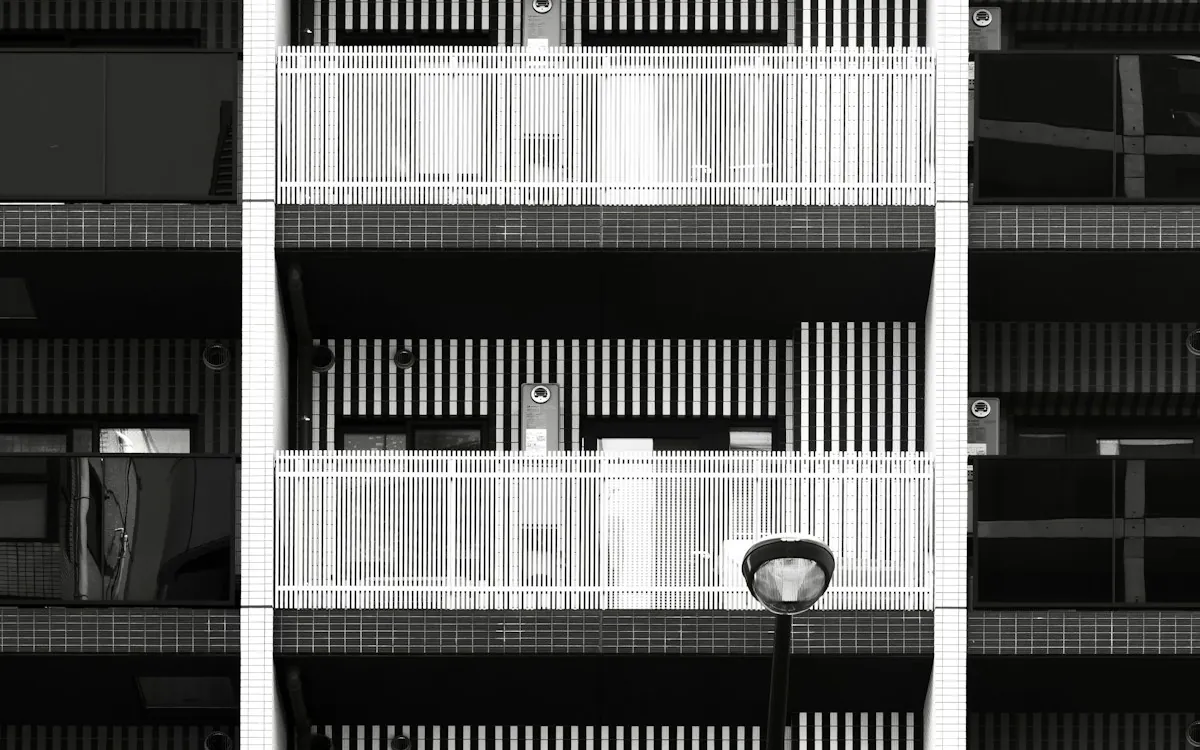 Black and white facade of an apartment building with white balconies and a street lamp