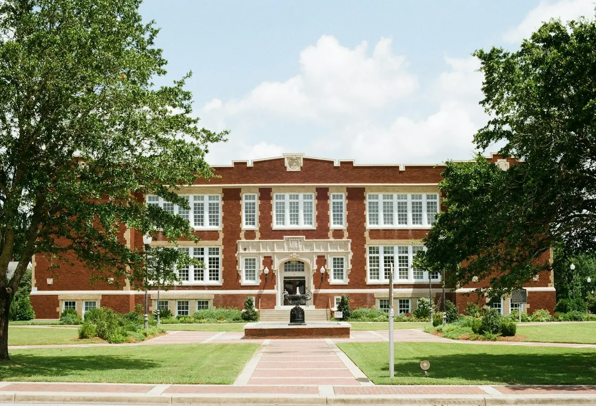 Older red brick institutional building with tall windows and a lawn