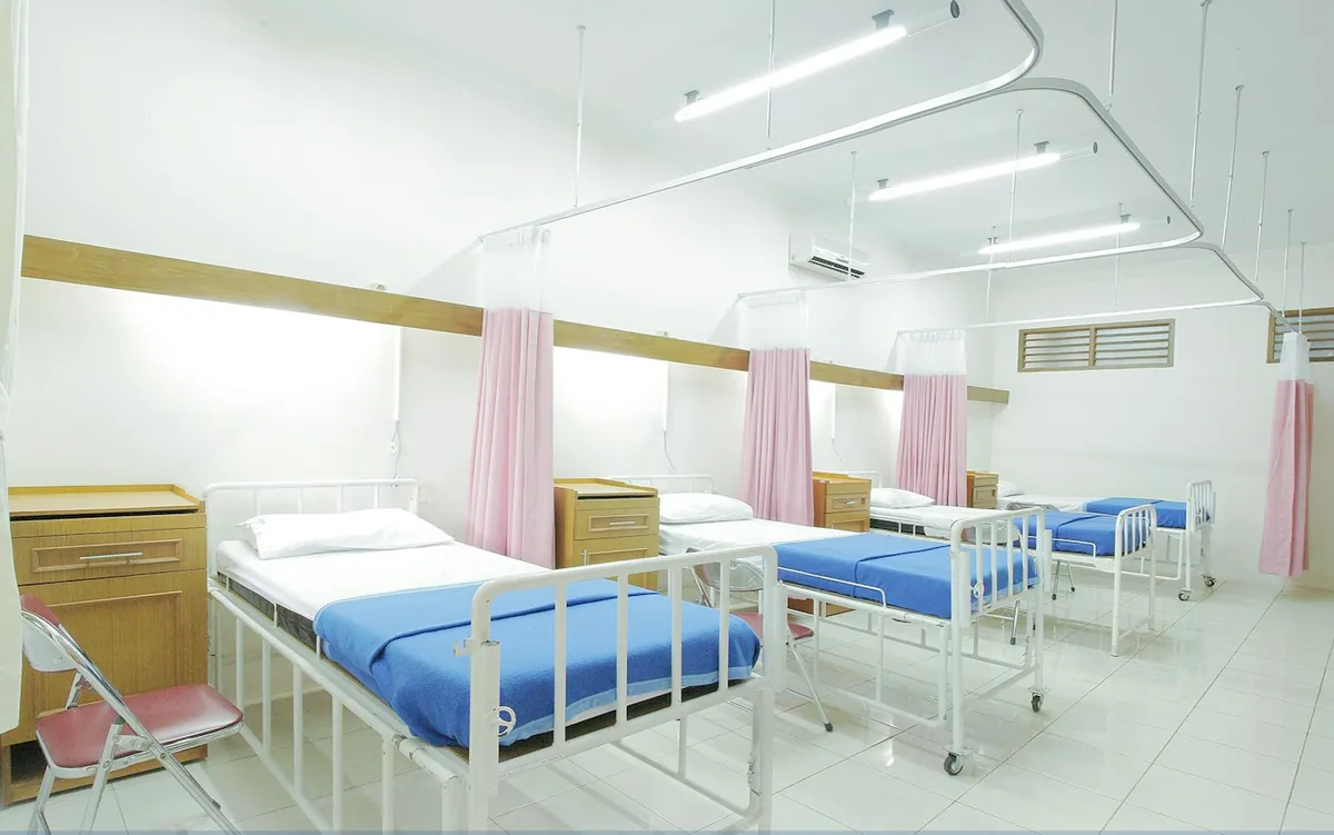 Bright hospital ward with rows of beds, blue sheets and pink curtains