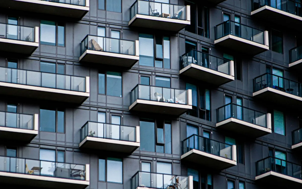 Tall residential tower with rows of balconies and blue glass against a dark sky