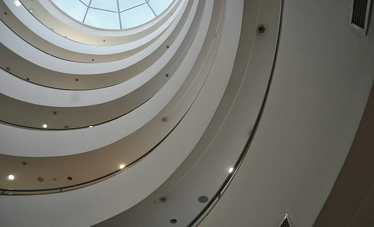 Curved white concrete atrium rings seen from below with a round skylight