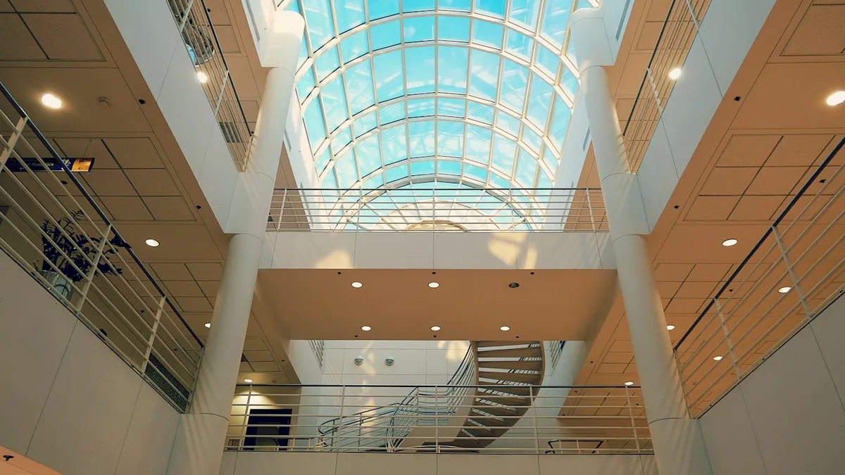 Glass-roofed office atrium with white columns, railings and a spiral stair below