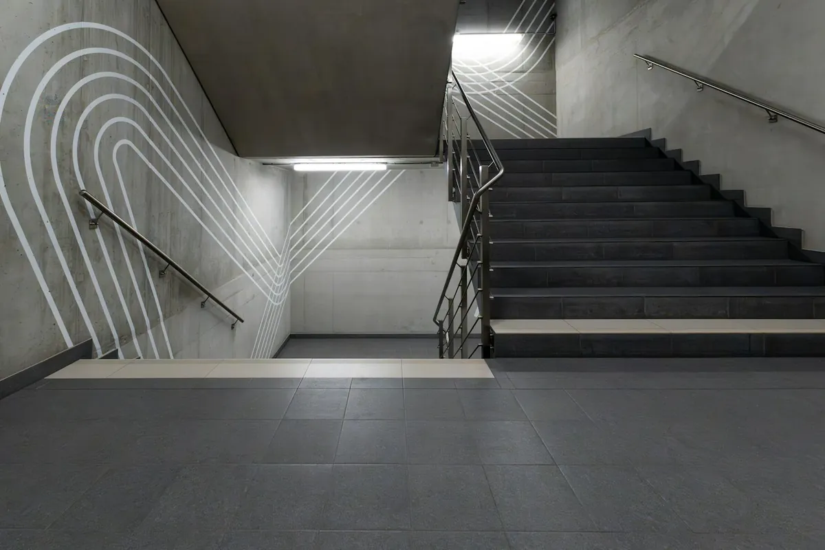 Concrete stairwell with white curved stripes on the wall and fluorescent lights
