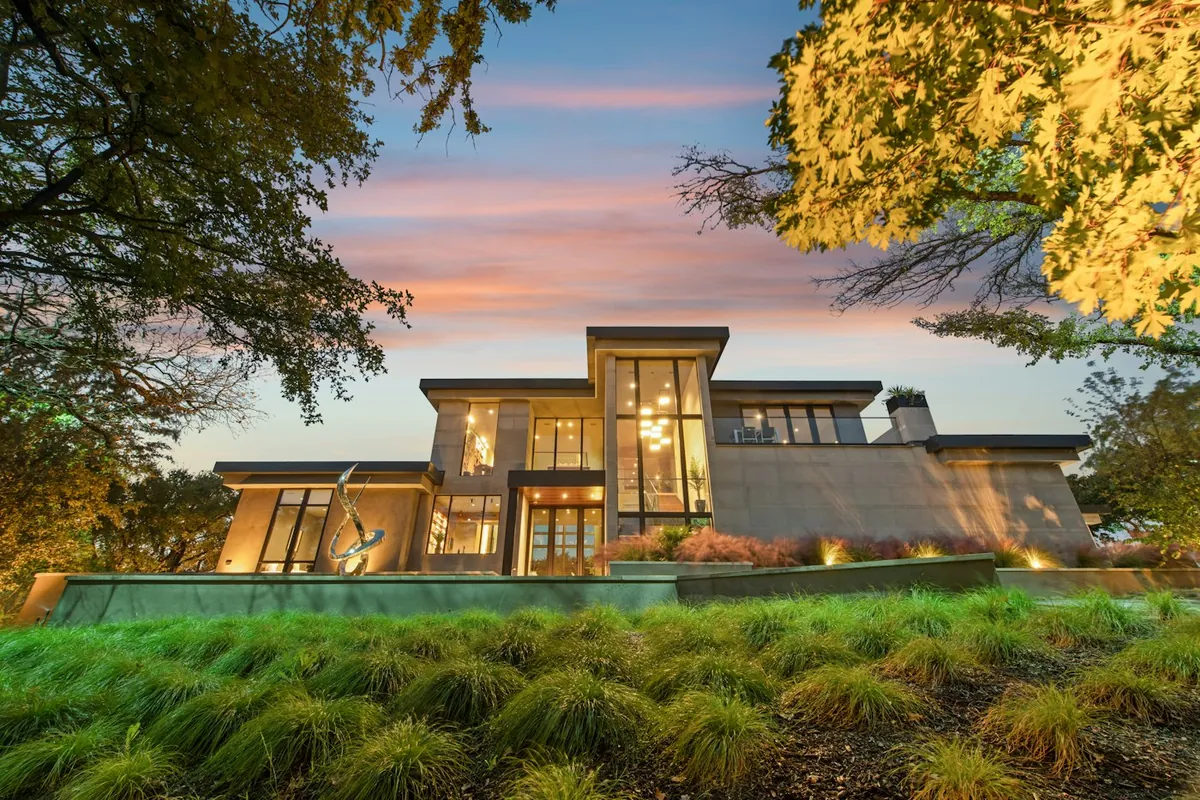 Contemporary glass-fronted house at dusk with orange sky and lush lawn