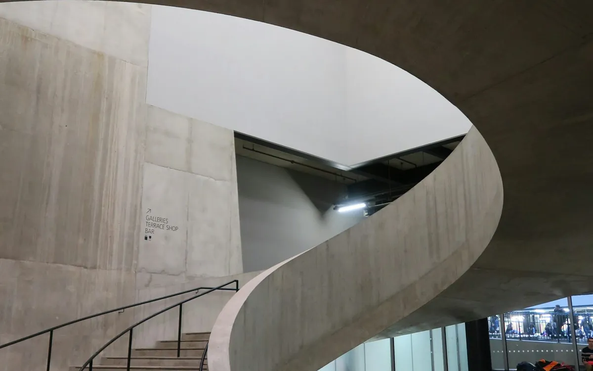 Grey concrete spiral staircase and railing inside a large modern hall