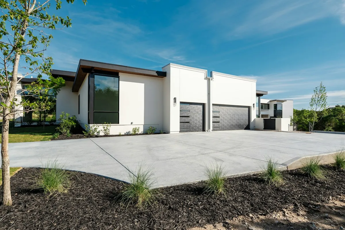 Modern white house with garage doors, a concrete driveway and clear blue sky