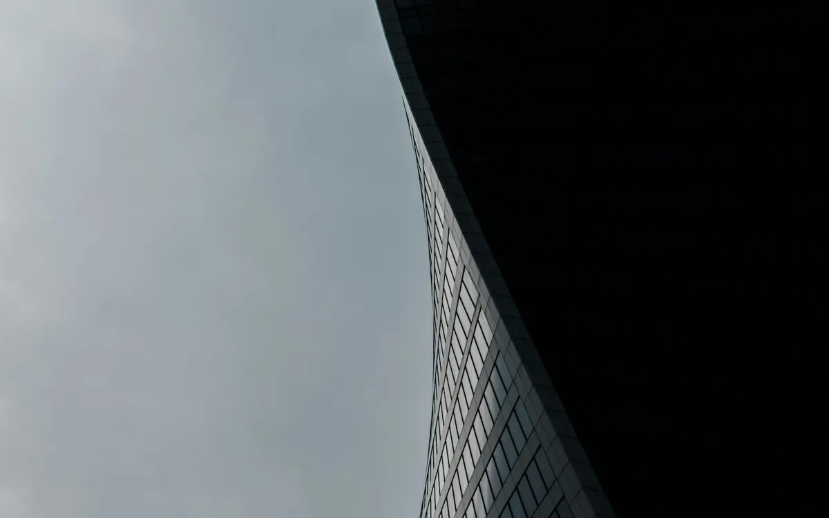 Dark curved glass tower leaning against a grey sky