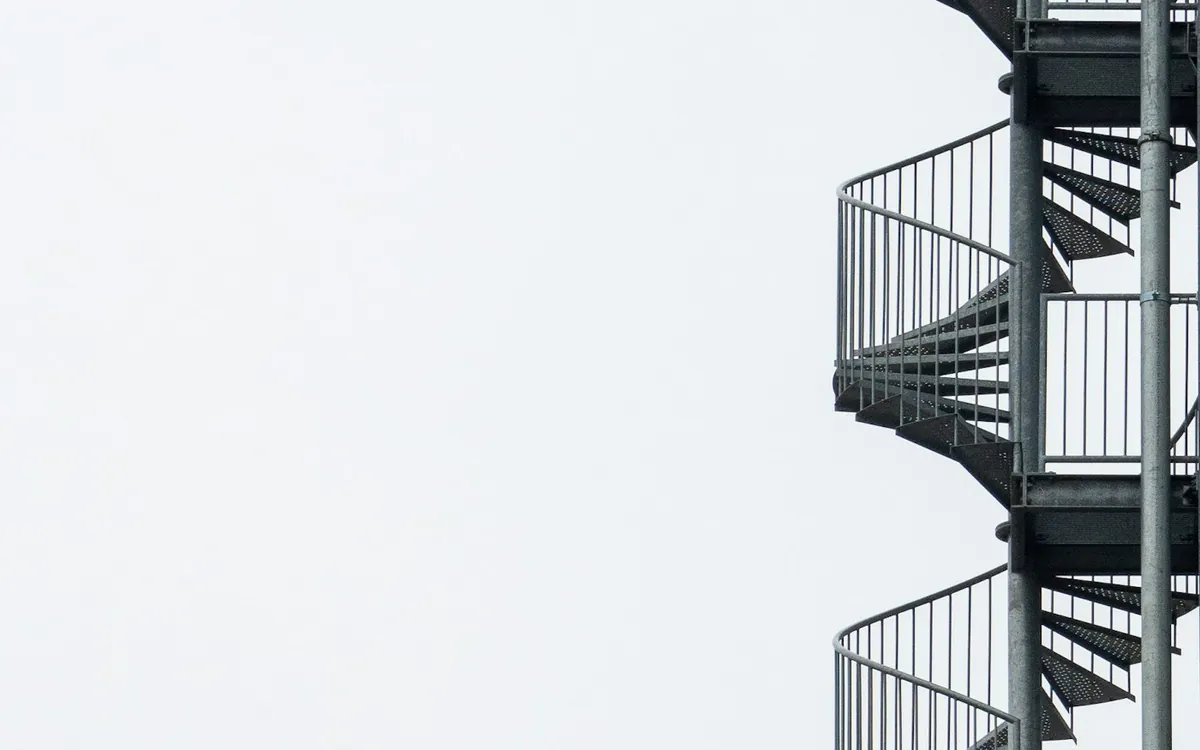 White metal exterior fire stairs rising up a pale wall