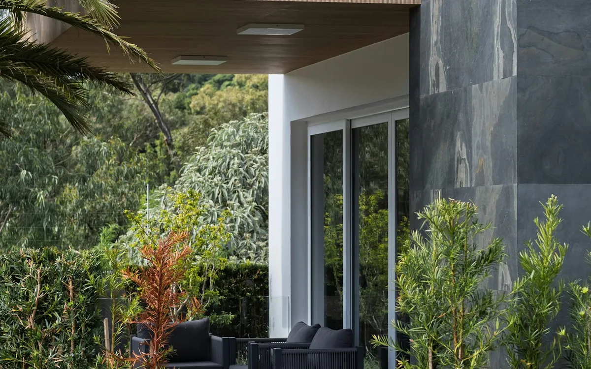 Garden terrace of a modern house with a timber-clad overhang and lush planting