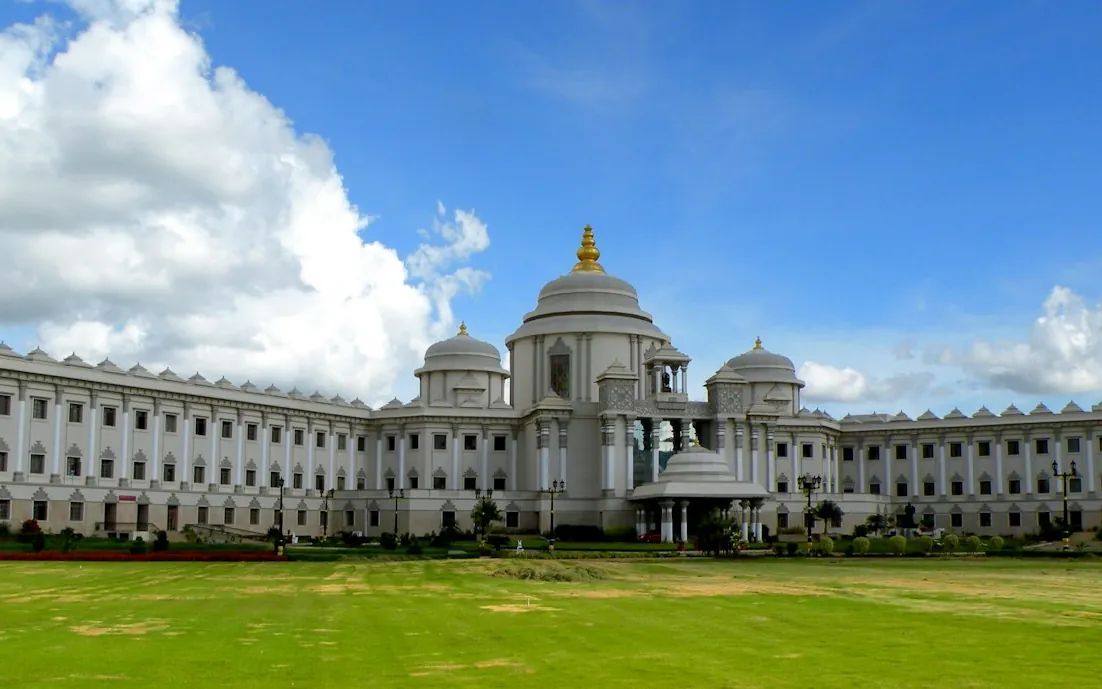 Wide view of a grand domed building with a green lawn under clouds in Bangalore