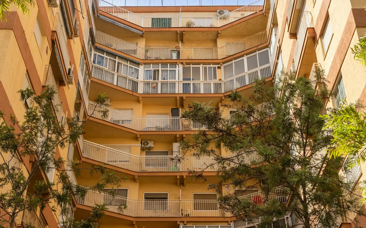 Residential courtyard with balconies and green trees under a blue sky