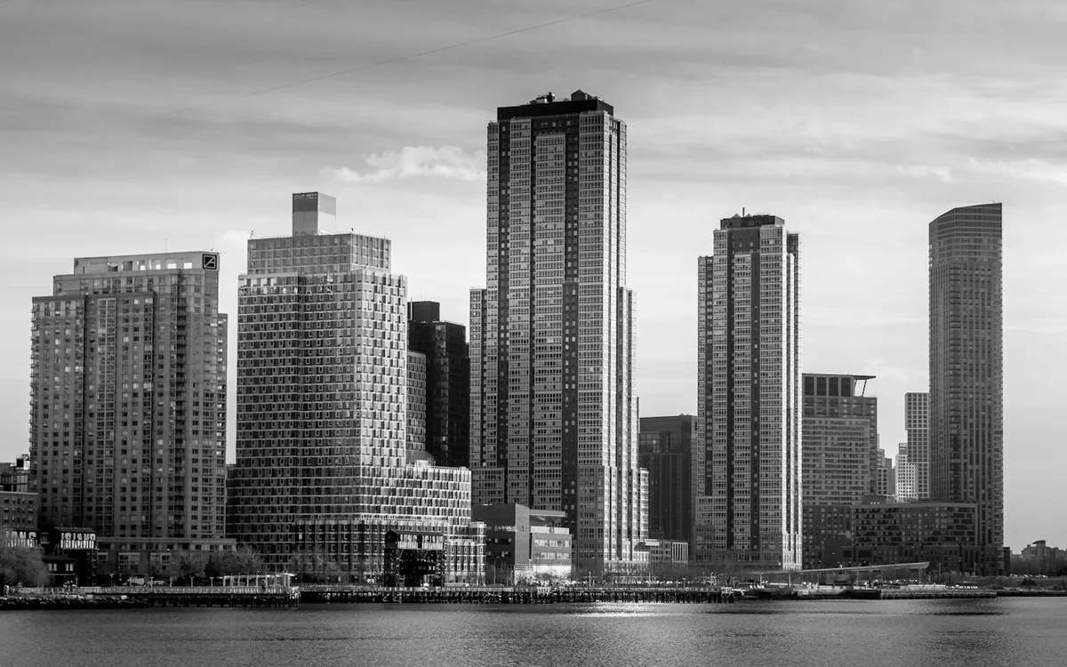 Black and white skyline of tall residential towers rising above a calm river